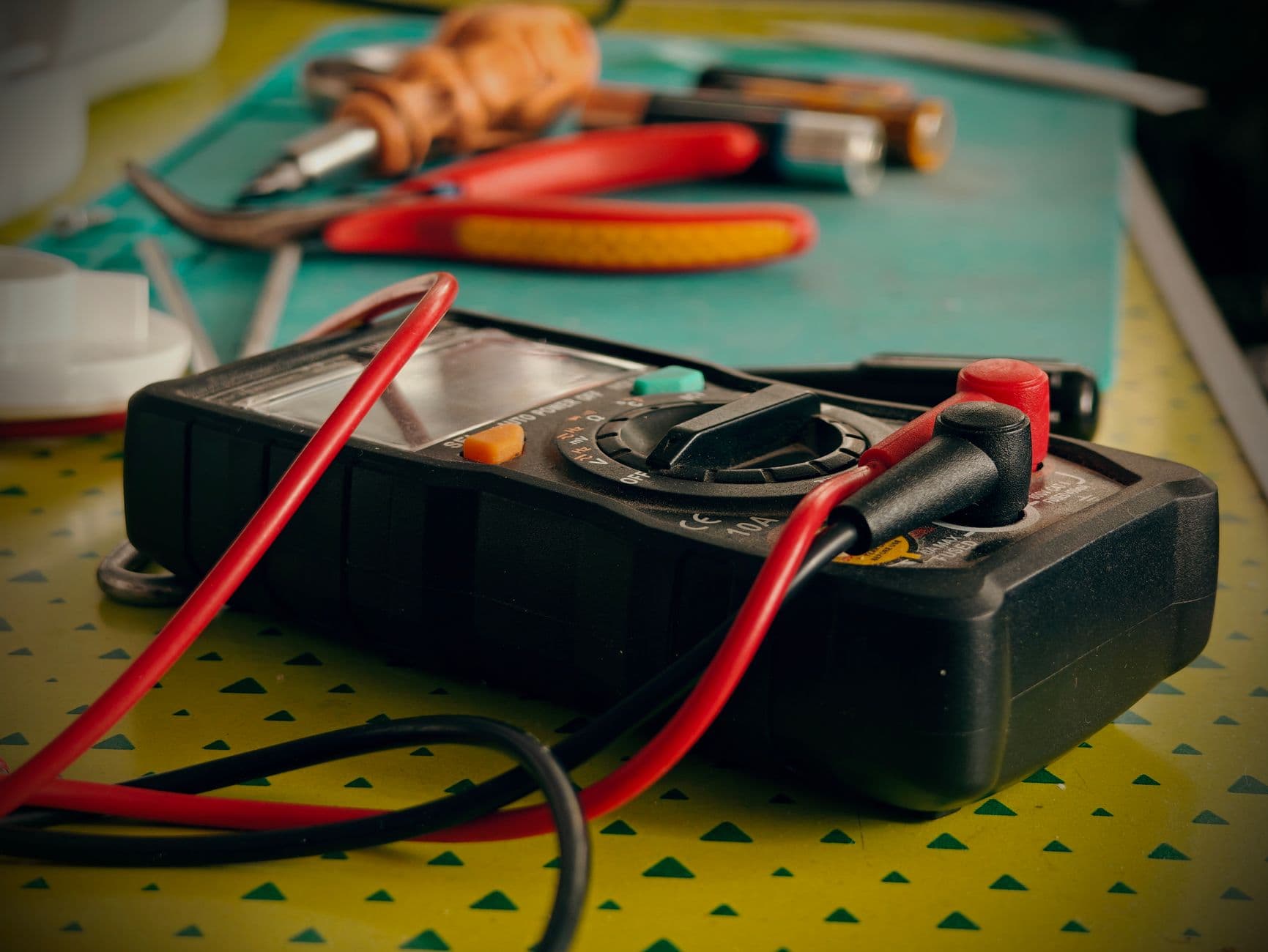 A multimeter and hand tools on a workbench